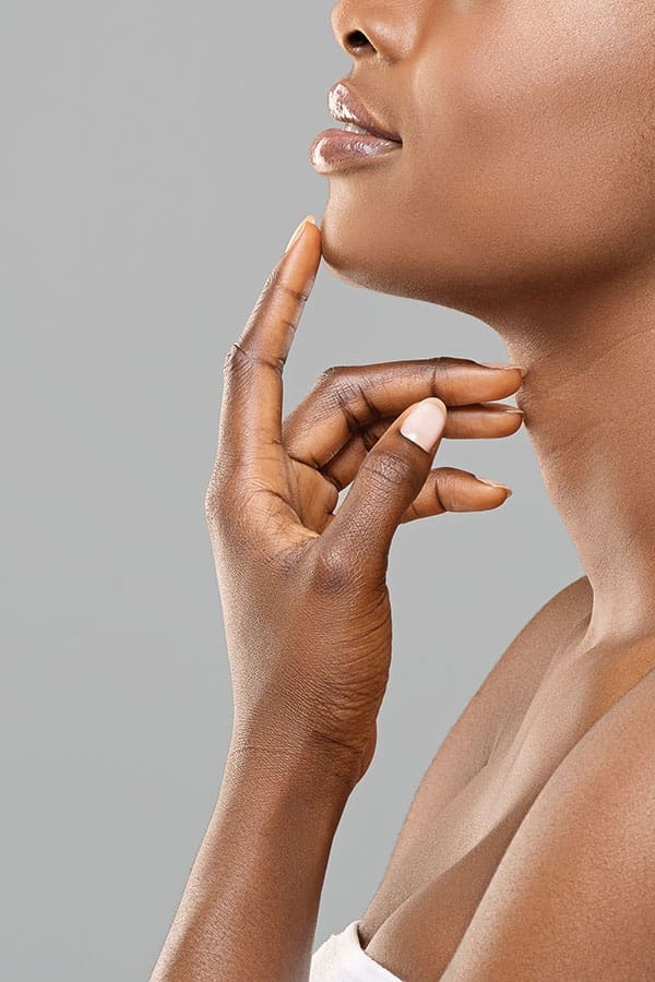 Chin augmentation. Unrecognizable afro woman touching implant in her face, happy with result of plastic surgery, gray background with free space