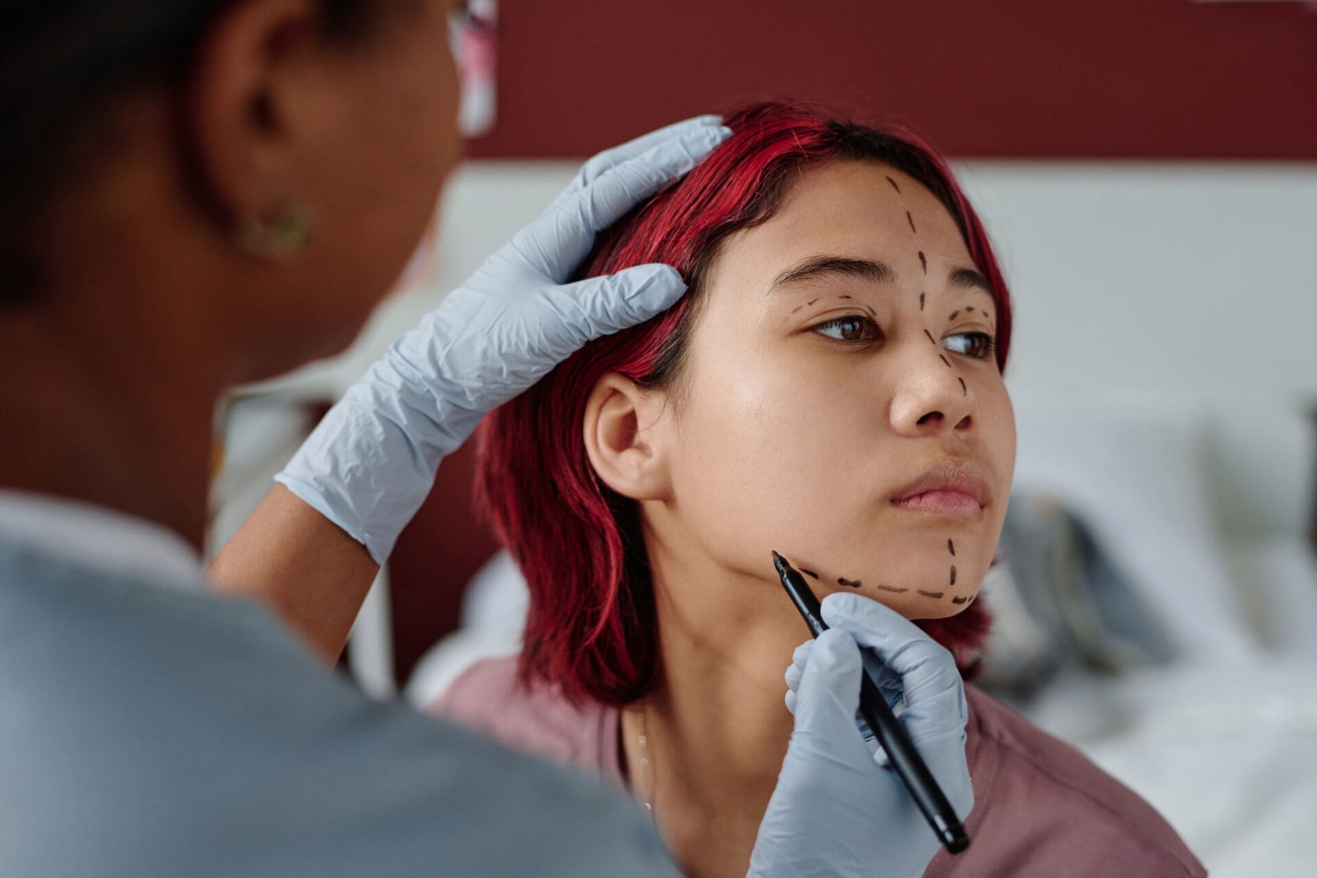 Gloved hands of young professional plastic surgeon drawing liftmarks Gloved hands of young professional plastic surgeon with highlighter drawing liftmarks on face of cute teenage girl in clinics